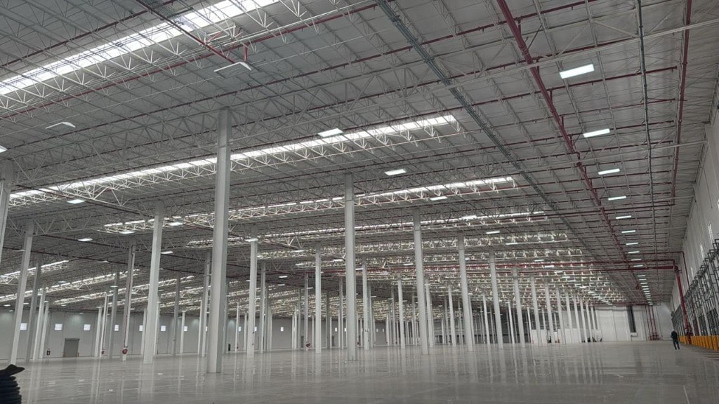 Interior de nave logística de gran altura: piso pulido, tragaluces, iluminación industrial y tubería contra incendios — espacio listo para alto volumen