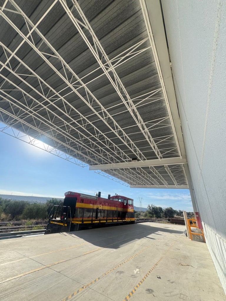 Andén intermodal con locomotora de carga bajo techumbre metálica y cielo despejado — cobertura nacional
